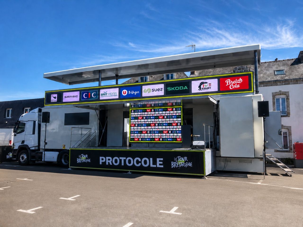 Car-Podium Organisa-Son déployé en plein soleil, scène avec bandeau LED sponsors sur le Tour de Bretagne