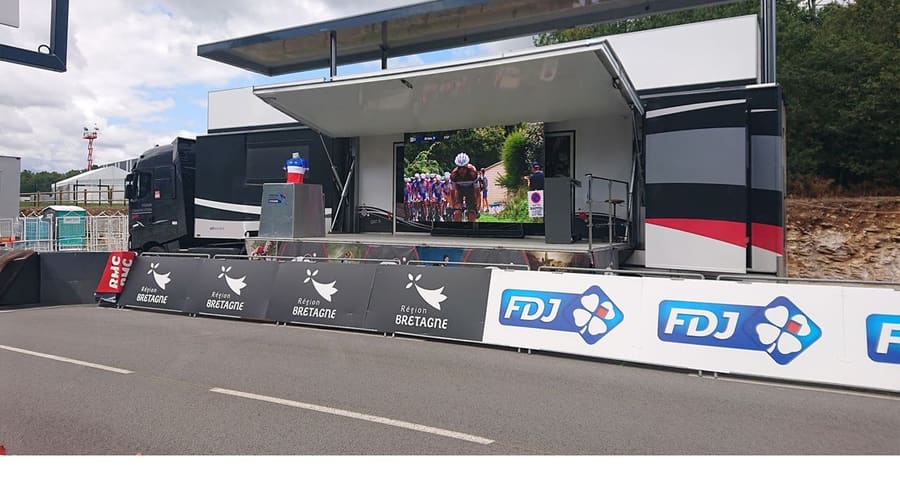 Scène du Car-Podium avec écran LED diffusant une course cycliste en direct
